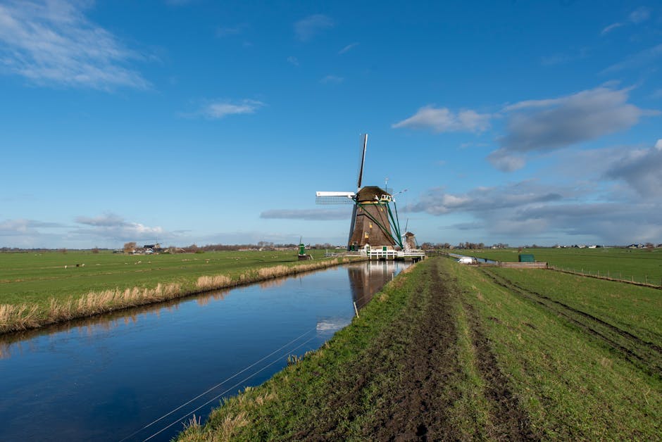 Scenic view of a historic windmill by a canal in Aarlanderveen, Holland, under a blue sky.