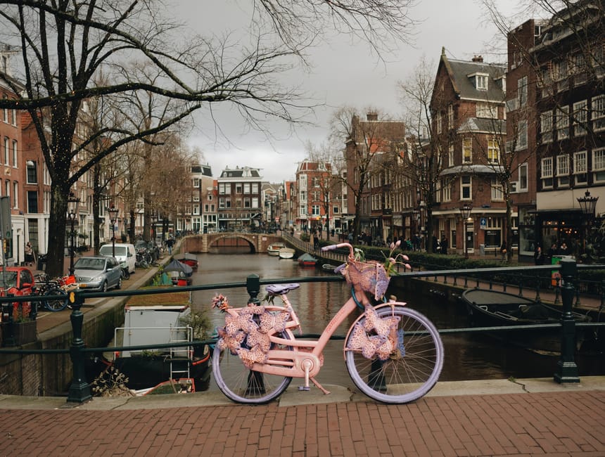 A picturesque Amsterdam cityscape featuring a canal, historic townhouses, and a decorative pink bicycle.