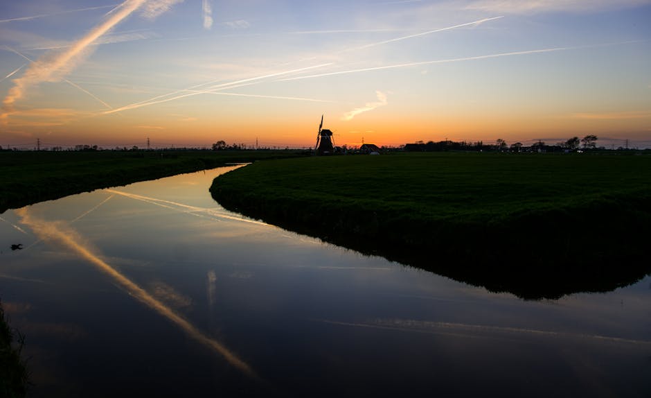 Serene sunset view with a windmill reflected in calm waters, capturing a classic Dutch landscape.