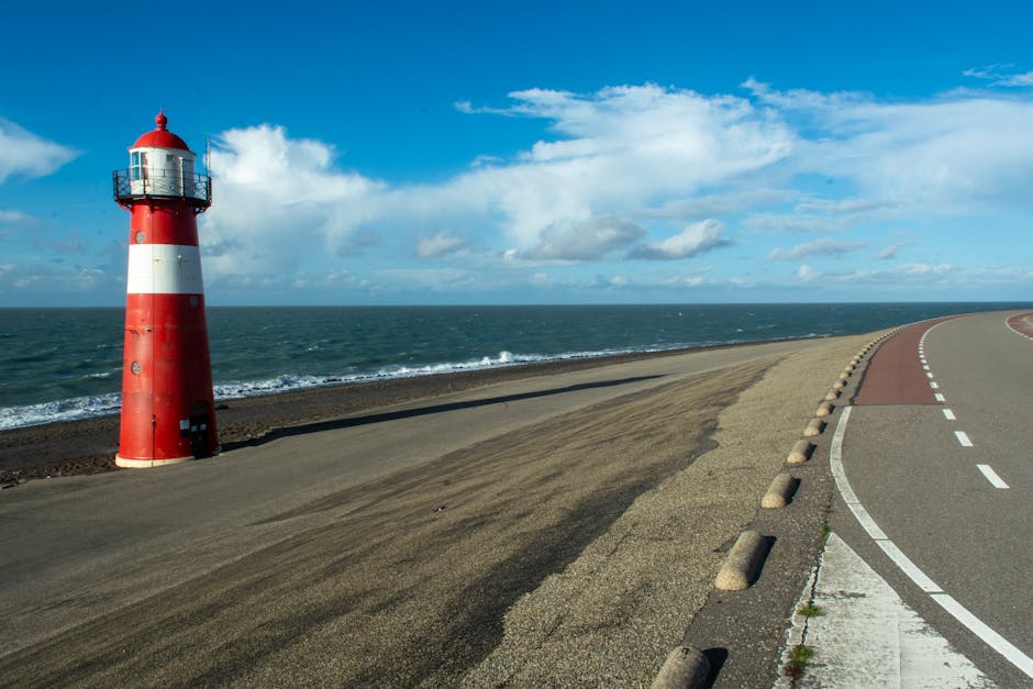 Lighthouse by the sea at Westkapelle, Zeeland, showcasing a winding road and bright sky.